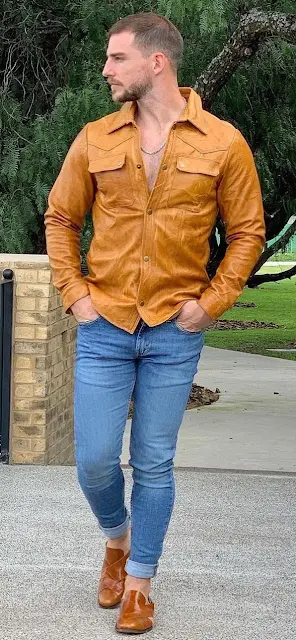 Man wearing blue jeans and orange leather shirt and Boots walking down the street