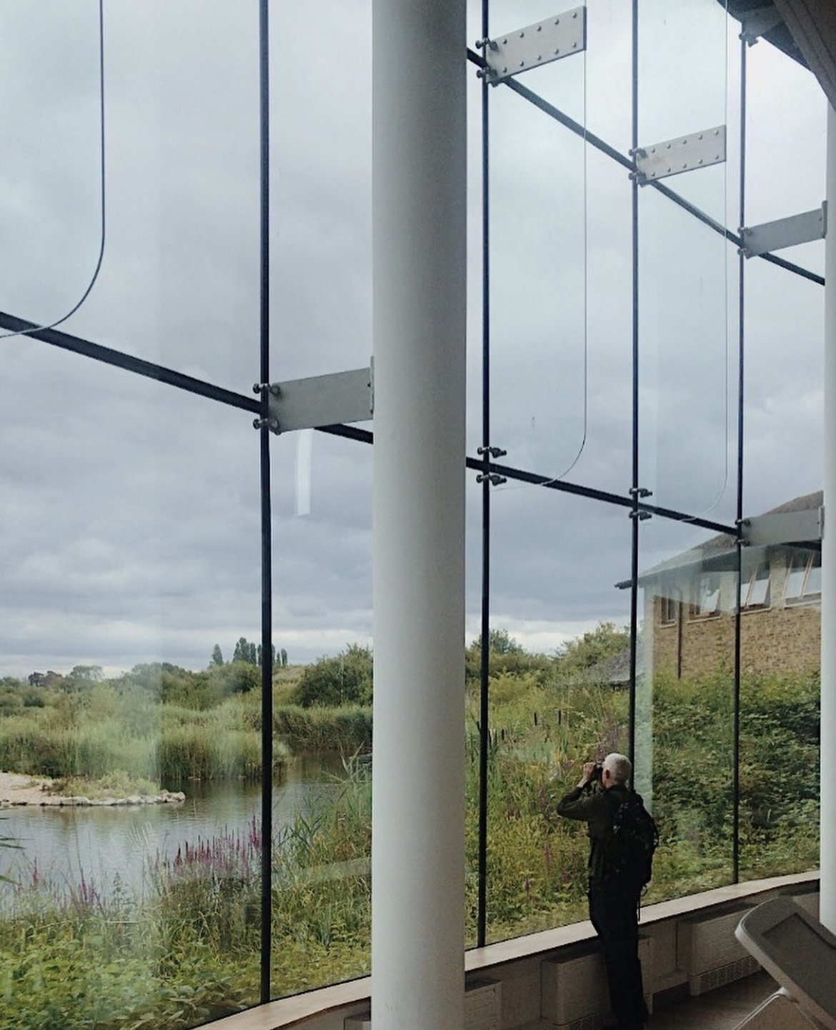 A man looks out of binoculars as a wetland's landscape through a big two storey window.