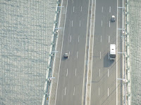 Looking down at the traffic on the road deck of the Akashi Kaikyo Bridge from the top of one of the main towers. The main cables are not visible but heaps of the supporting cables that attach the main cable to the roadway are visible.