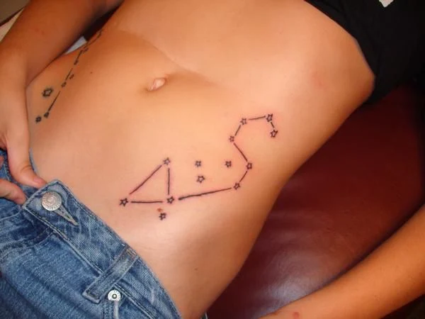 chica acostda, vestida con tejanos lleva tatuaje de la constelación de leo en la cadera