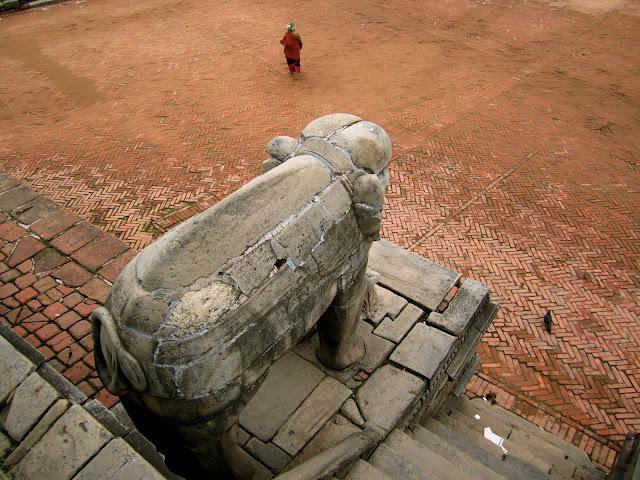 A stone elephant looks out over the red square as a woman walks past.