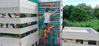 Eduardo Kobra - Da periferia de São Paulo para o mundo. Nascido em 1975 no Jardim Martinica, bairro pobre da zona sul paulistana, o artista Eduardo Kobra tornou-se um dos mais reconhecidos muralistas da atualidade, com obras em 5 continentes.   Sobre o mural  O muralista brasileiro Eduardo Kobra, 45 anos, finalizou na sexta-feira (22 de janeiro), um grande mural, em uma empena(Empena é a parte superior das paredes externas, acima do forro, fechando o vão formado pelas duas águas da cobertura. Cada uma das paredes laterais onde se apoia a cumeeira os telhados de duas águas) do Colégio Ser! (à Rua Doutor José Aleixo Irmão,301, no Alto da Boa Vista, em Sorocaba). Com 22 metros de altura por 11 de largura, o mural, mostra um menino subindo por uma escada encostada a uma estante em uma biblioteca à procura de um livro. Para o mural, Kobra, que pintou acompanhado por dois artistas de sua equipe, Agnaldo Brito e Marcos Rafael, utilizou 350 latas de spray e 20 galões de esmalte. O processo foi realizado em 20 dias, com muitas dificuldades devido às chuvas intensas durante o período. Esse mural é o primeiro de Kobra em 2021.  Descrição: Foto. Céu azul com nuvens. Na fachada de um prédio localizado entre outros dois de concreto com vidros espelhados,o da esquerda é mais alto, o mural com um menino de cabelo escuro,com os pés apoiados no alto de uma escada de madeira, está junto à uma estante. Ele firma a mão esquerda na lateral esquerda da escada, estica o braço direito e alcança um livro,na quinta das seis prateleiras, repletas de livros multicoloridos. O menino usa camiseta cinza. O colorido das grossas lombadas dos livros se reproduz nos braços, bermuda, pernas e tênis do menino. Ao fundo, vegetação densa.