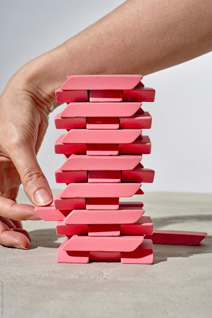 Jenga con gomas de borrar de color rosa. Una mano cuidada de mujer está sacando una pieza de la base. Ya hay otras fuera.