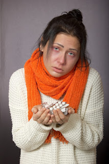 صورة لفتاة تعاني من الزكام حاملة في يدها أقراص من المضادات الحيوية