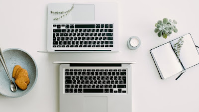 White top online work station with two computers, a notepad and a bowl of cookies.