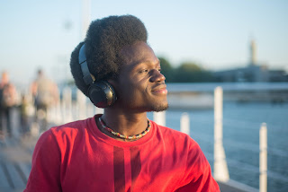 young black man listening on headphones near the waterfront.