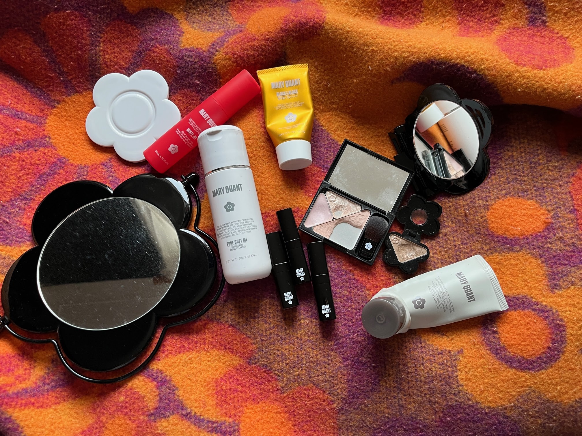 A flatlay of Mary Quant makeup and skincare including mirrors, lipsticks, suncream and skincare.