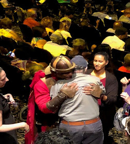 A person dressed as Roman soldier, a Deafblind man, and a woman hug each other