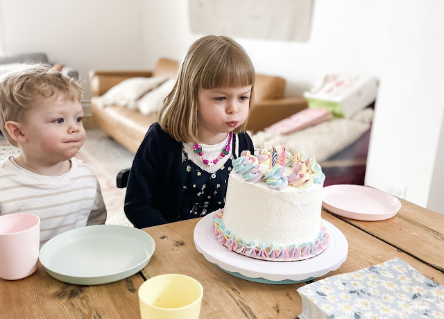 two young children blowing the candles out on a cake that is decorated in rainbow swirls
