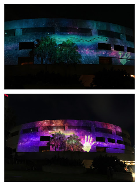 Projections of an animated eel and white hand in different colors on facade of Hamer Hall