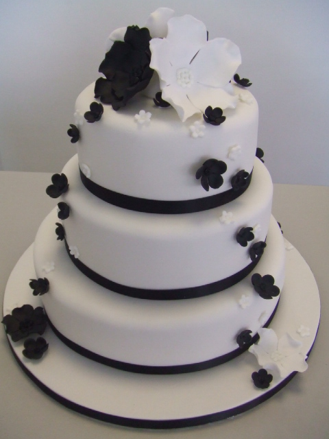 Three tier white cake with black ribbons and black and white flowers