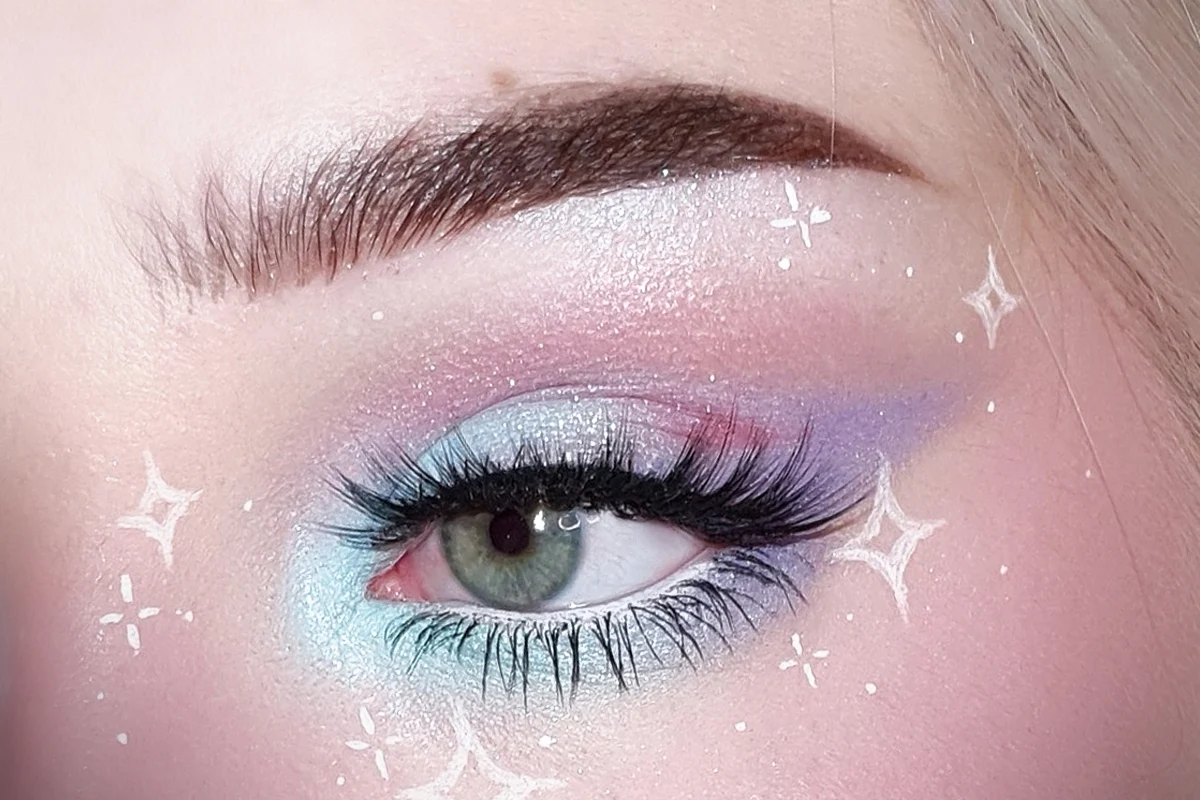 close-up of a blue eye with pastel goth makeup, long lashes and white faux freckles on the skin