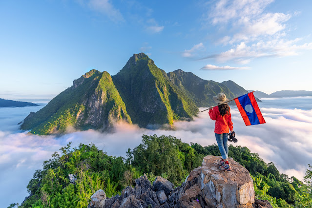 woman hiker carrying flag of laos on top of the mountain with fog on sunset