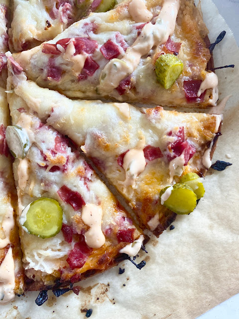 Close up shot of Reuben Pizza cut into slices baked on parchment paper.