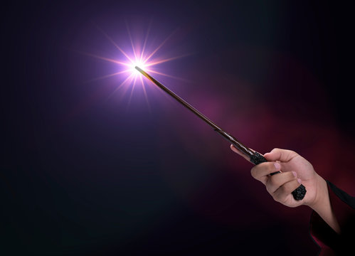 A person hold a wand with a purple magic spell in the black background