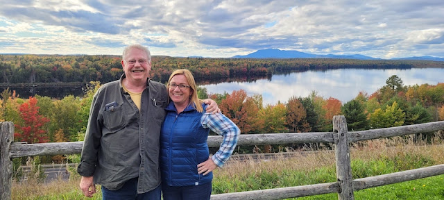 Couple posing in front of mountain and pond scenery.