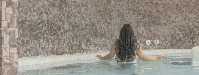 a girl stands waist-deep in a crystal clear indoor pool.