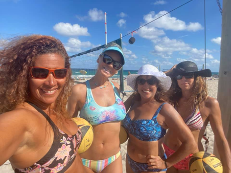 Four women on the beach in front of a beach volleyball court