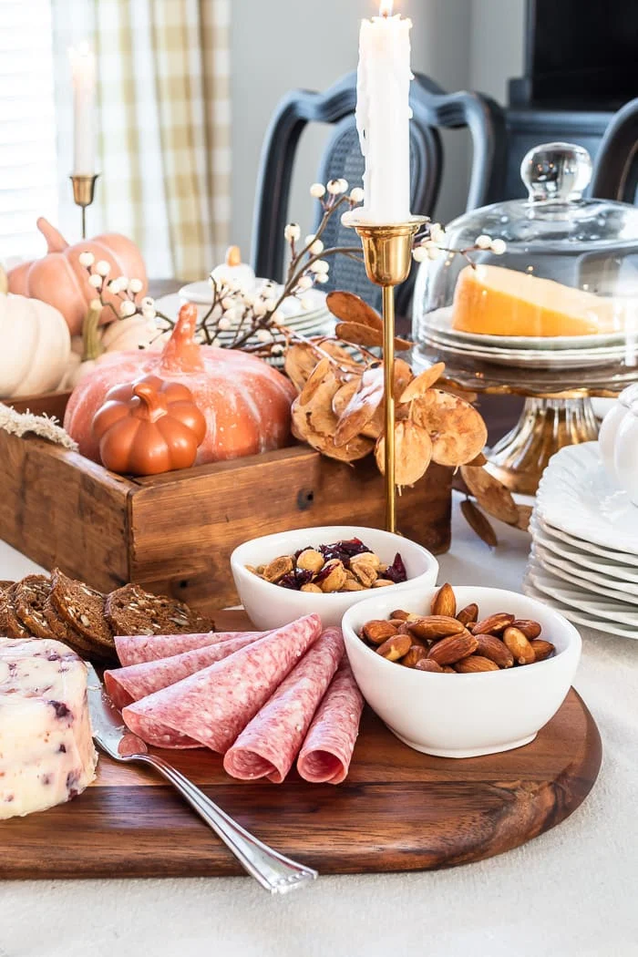 charcuterie board on fall decorated dining table with candles, pumpkins, berries, leaves, wood