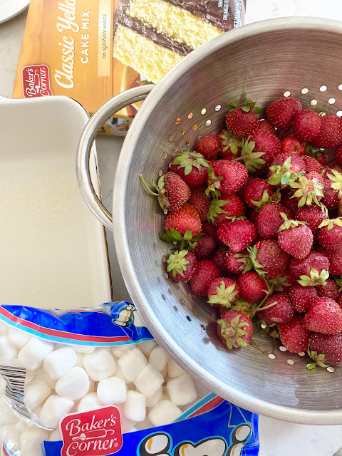 Colander of fresh strawberries, marshmallows, yellow cake mix and a baking dish.