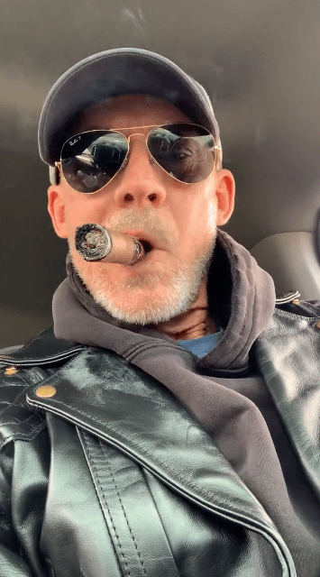 Animation sitting in driver seat wearing shiny black biker leather jacket smoking cigar sporting sunglasses