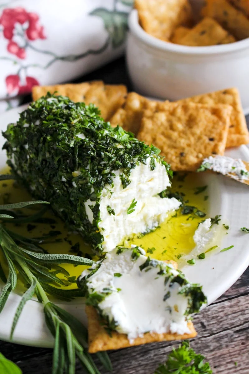 Side view of Herb and Olive Oil Goat Cheese Log on a cream colored plate with crackers next to it.