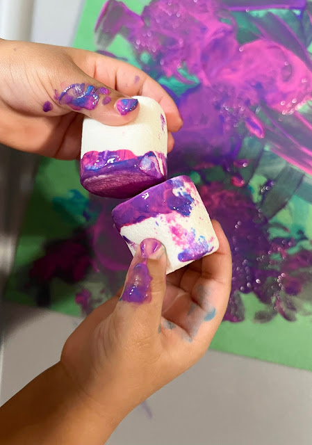 a childs hand holding two marshmallows with paint on them.