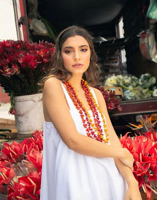 Model wearing a long white dress and eco-friendly necklaces made from native Amazonian seeds. Explore our site to support these indigenous artisans by purchasing one of these necklaces.
