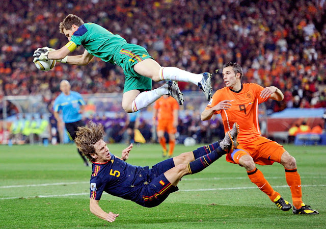 Casillas bloca espectacularmente un balón llevándose por delante a Puyol ante el acoso de Van Persie. SELECCIÓN DE ESPAÑA 1 SELECCIÓN DE PAÍSES BAJOS 0 Domingo 11/07/2010, 20:30 horas. XIX Copa Mundial de Fútbol Sudáfrica 2010, Final. Johannesburgo, Sudáfrica, estadio Soccer City: 84.490 espectadores. GOLES: 1-0: 116’, Iniesta. ESPAÑA GANA EL CAMPEONATO MUNDIAL DE FÚTBOL.