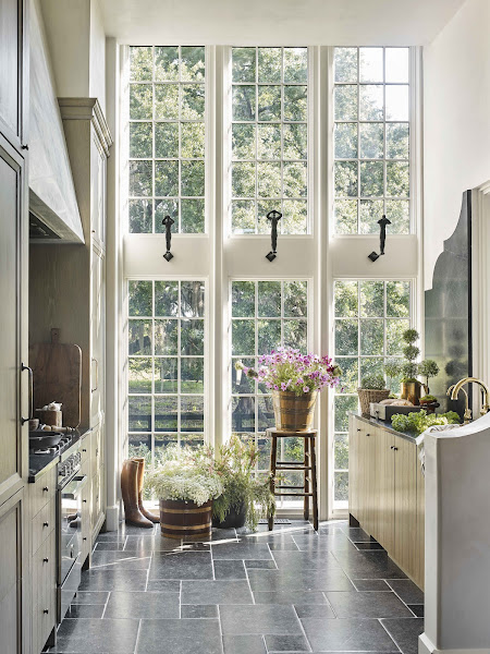 una pared de ventanas trae luz natural a una cocina de galera con encimeras y pisos de piedra