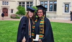 Two women wearing graduation gowns and hats, discuss academic degree and terminal academic degree.