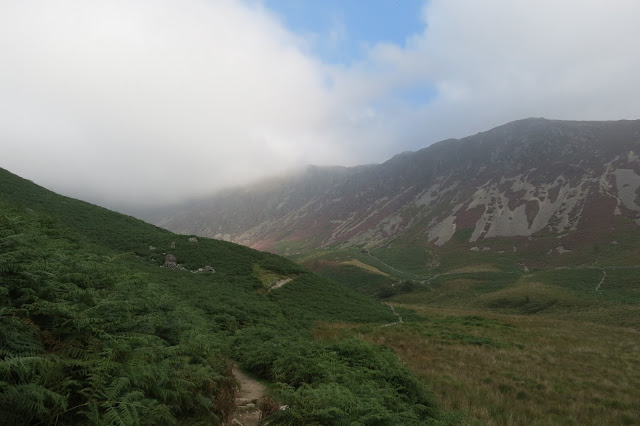 A mountain ridge part hidden in cloud, which is breaking to reveal blue sky.