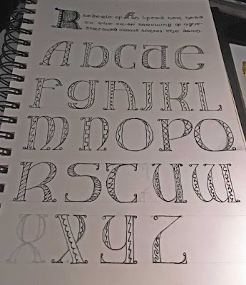 A sketchbook page with the alphabet in outlined capital letters on five lines, in a semi-Uncial style. Each letter has a different division line in the uprights, including zigzags, curves, crenellations, and diamonds. A more decorated capital 'R' is at the top of the page, with three lines of text below.