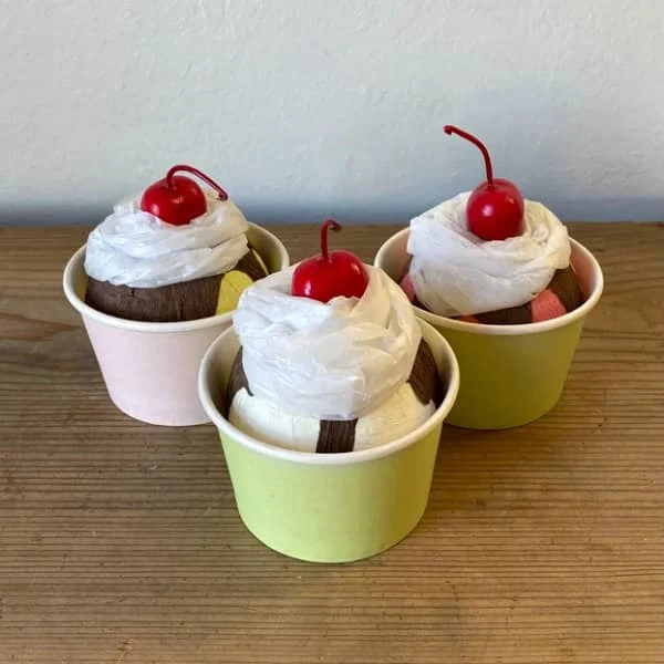 three ice cream sundaes with whipped cream and cherry on top, each displayed in a small pastels cups