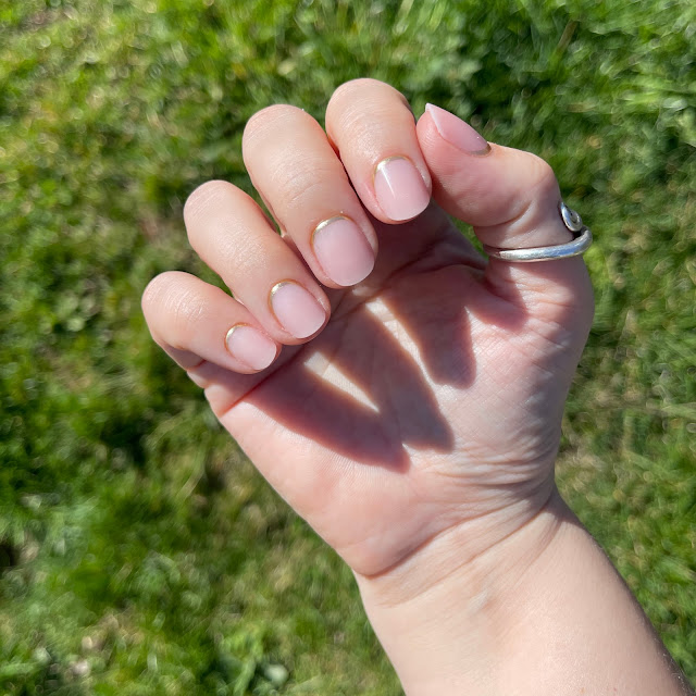 Glamnetic nails after application that have been filed and trimmed on woman's hand over grass in the sun