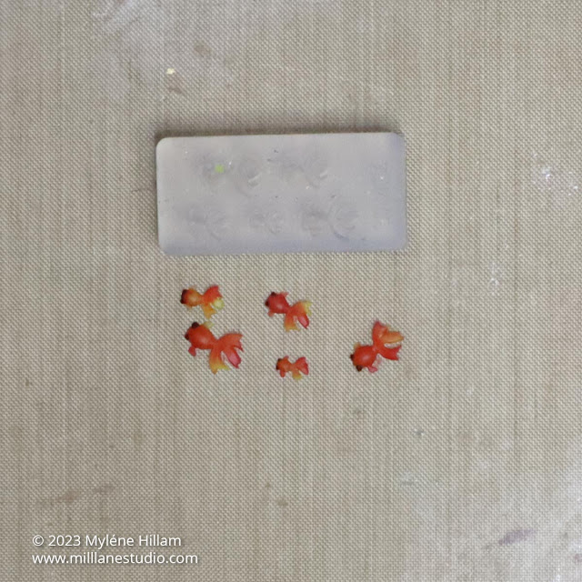 Five mini resin goldfish on a teflon craft sheet next to the silicone goldfish mould