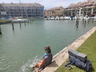 Murille sits on a wall, her feet are in the water of a harbor