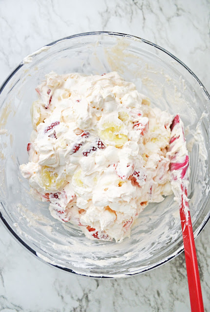 Strawberry Banana Cheesecake Fluff Salad being stirred in a clear glass bowl.