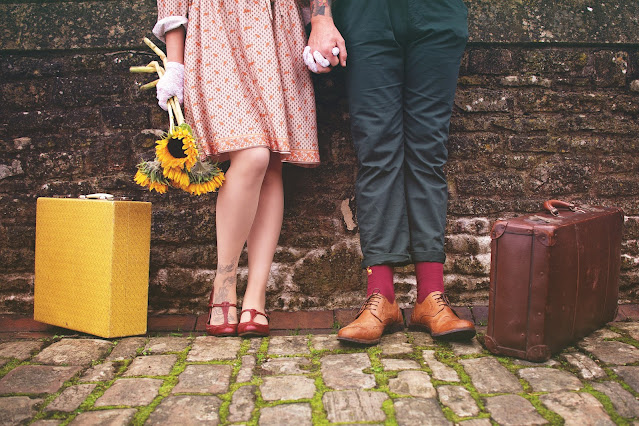 A young lady and a man hold their hands and try to get married. Lady has sunflowers in one hand. Two bags are on the floor.