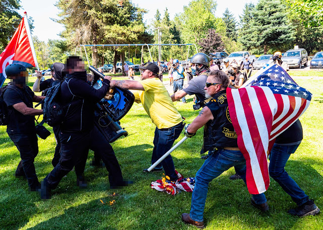 Physical confrontation between two groups of men in a park, with one group holding an American flag