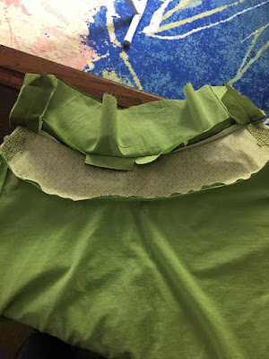 The guts of a green skirt's three-layered waistband, with apple-green lining fabric pinned to the lower edge of the bottommost layer.