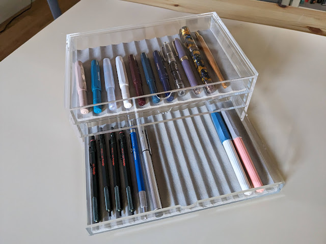 An acrylic transparent box with drawers filled with pens.