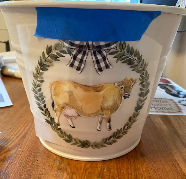 Photo of a cow decor transfer being added to a bucket front.