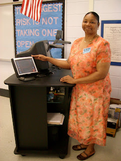 african american student with peach spring dress with mint green flowers design she is standing besides the black codex equipment in the access lab.