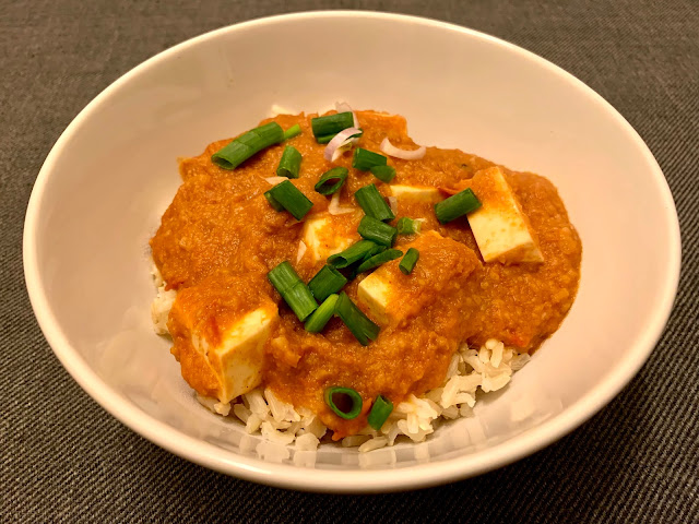 Bowl of paneer butter masala over rice, topped with spring onion