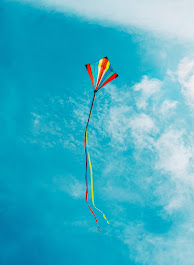 Image of a vertically striped kite flying against a blue sky with puffy white clouds