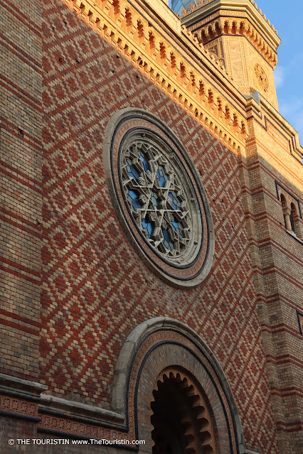 A rose window on the facade of a red and cream-coloured synagogue decorated in Moorish style.