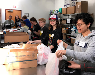 8 people stand at a table bagging food from various boxes