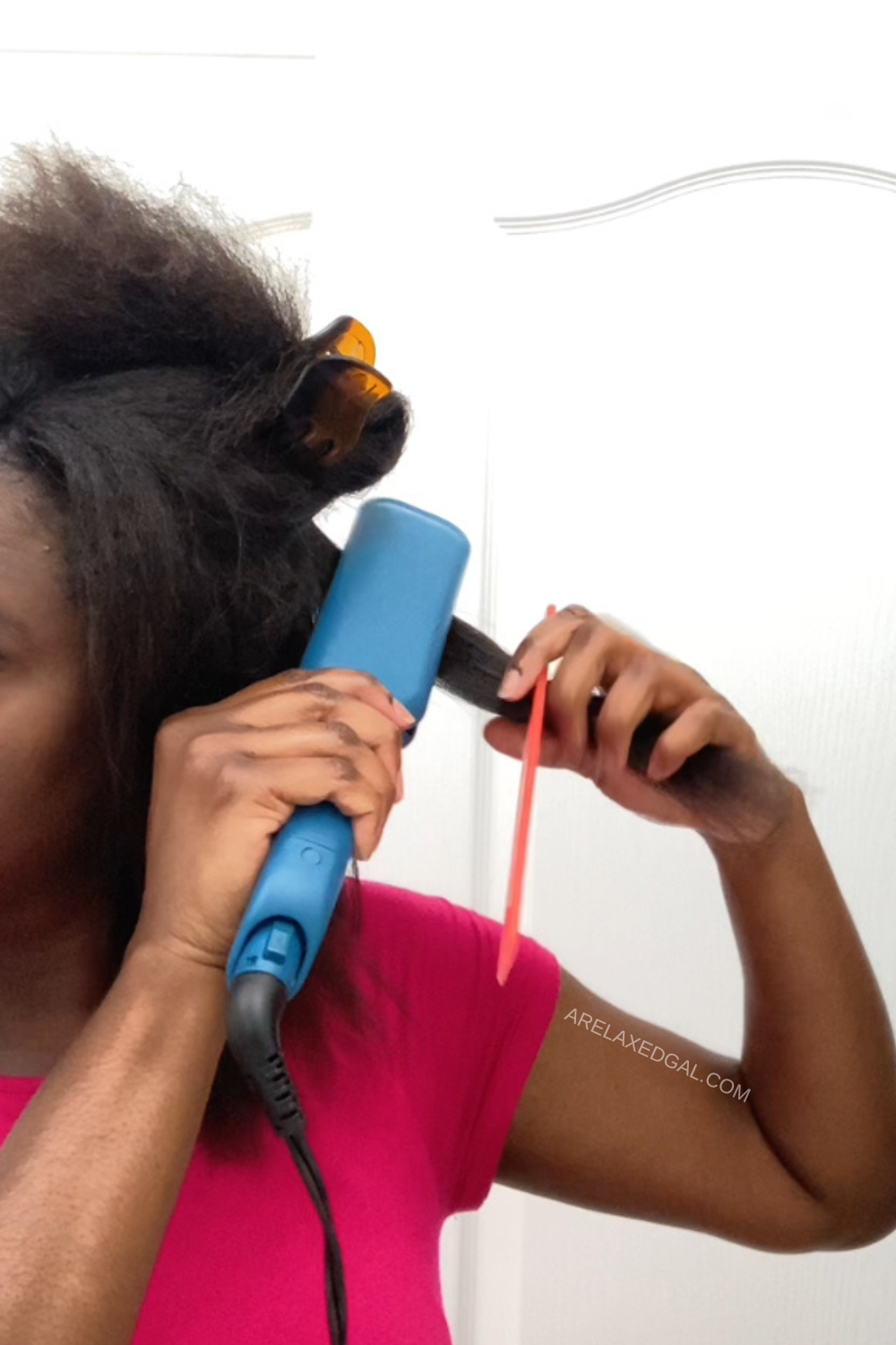 woman with relaxed hair flat ironing a section of hair using a blue flat iron.