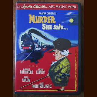 DVD cover of Murder, She Said. An older woman stands to the side while a train passes.